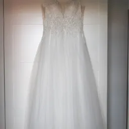 Elegancka suknia ślubna z koronkową górą i tiulowym dołem, wisząca na wieszaku z napisem 'Żona' na tle białej szafy.