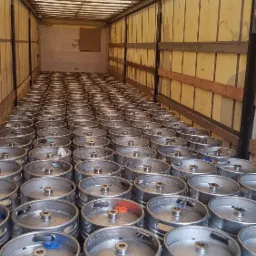 Wnętrze naczepy wypełnionej po brzegi metalowymi beczkami z piwem, widok z tyłu naczepy, oświetlenie górne