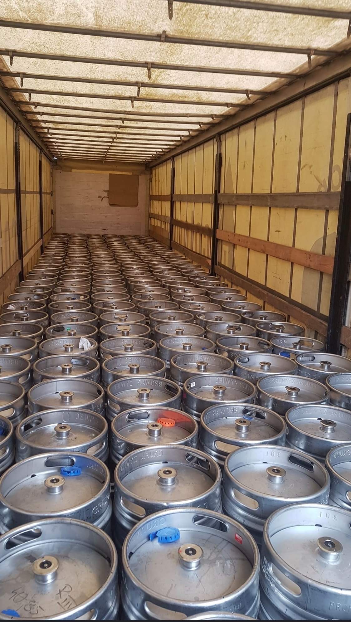 Wnętrze naczepy wypełnionej po brzegi metalowymi beczkami z piwem, widok z tyłu naczepy, oświetlenie górne