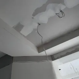 Sufit w trakcie remontu: widoczne fragmenty płyty karton gips, szpachlowanie, wystające kable elektryczne, przygotowanie do montażu oświetlenia.