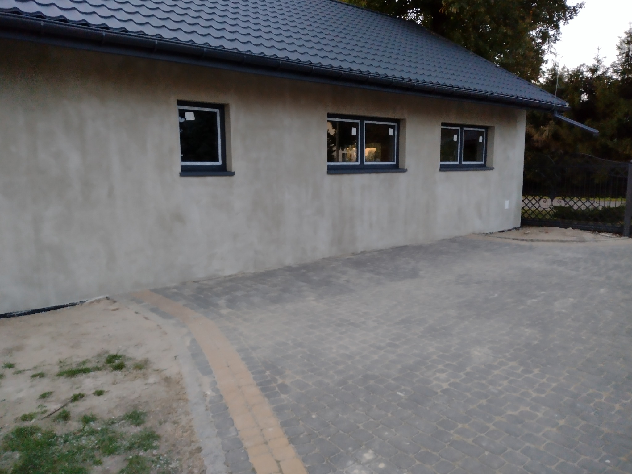 Dom po ociepleniu elewacji z nowymi oknami i szarym dachem, widok z zewnątrz na kostkę brukową.