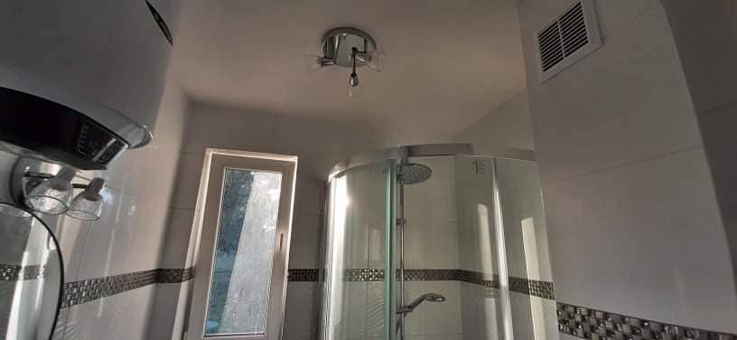 Nowoczesna kabina prysznicowa z hydromasażem, widok z dołu, na ścianie białe płytki z dekoracyjnym pasem, okno z widokiem na zewnątrz, bojler elektryczny.