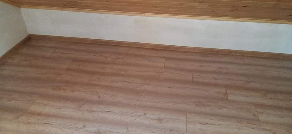 Ułożony parkiet laminowany w odcieniach brązu, widoczne listwy przypodłogowe i drewniana boazeria sufitowa.