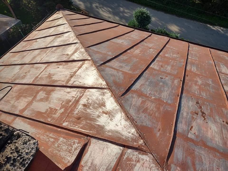 Metalowy dach w odcieniach czerwieni i bieli, z widocznymi śladami zużycia i wcześniejszych prac konserwacyjnych, sfotografowany z góry.