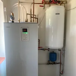 Biała pompa ciepła Nibe z podłączonym zasobnikiem ciepłej wody i niebieskim naczyniem przeponowym, zamontowana w kotłowni w Ostrowcu Świętokrzyskim.