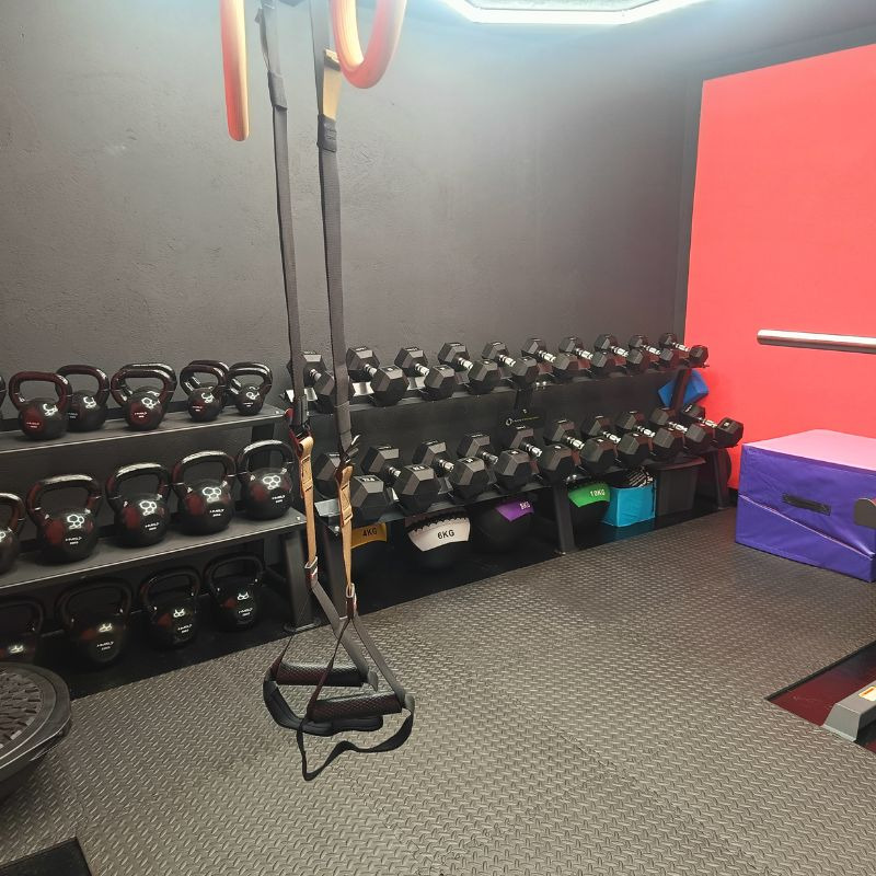 Profesjonalna siłownia: kettlebells, hantle, TRX, piłki lekarskie na tle szarej ściany i czerwonego akcentu. Sprzęt gotowy do treningu personalnego.