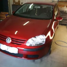 Czerwony Volkswagen Golf po renowacji lakieru we Wrocławiu, widoczny w warsztacie z oświetleniem halogenowym.
