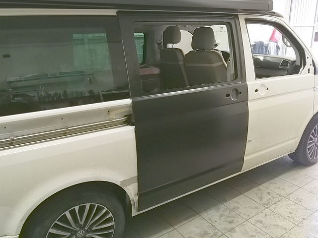 Biały van po częściowym nałożeniu podkładu na bok pojazdu, widoczne ślady szpachli i przygotowania do malowania.