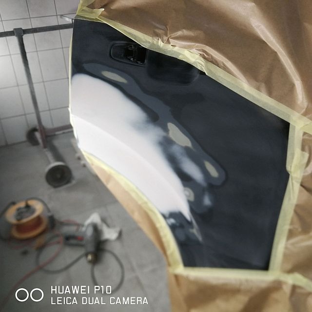 Przygotowany do lakierowania fragment karoserii samochodu, zabezpieczony papierem i taśmą, z widocznymi śladami szpachlowania.