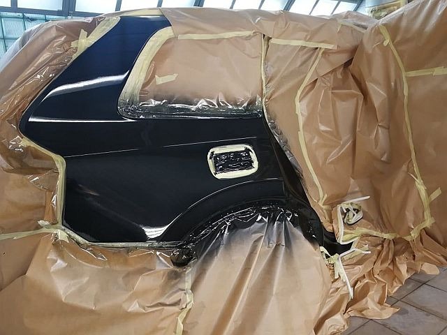 Część karoserii czarnego samochodu, zabezpieczona folią i taśmą malarską przed lakierowaniem, widoczne świeżo polakierowane elementy.
