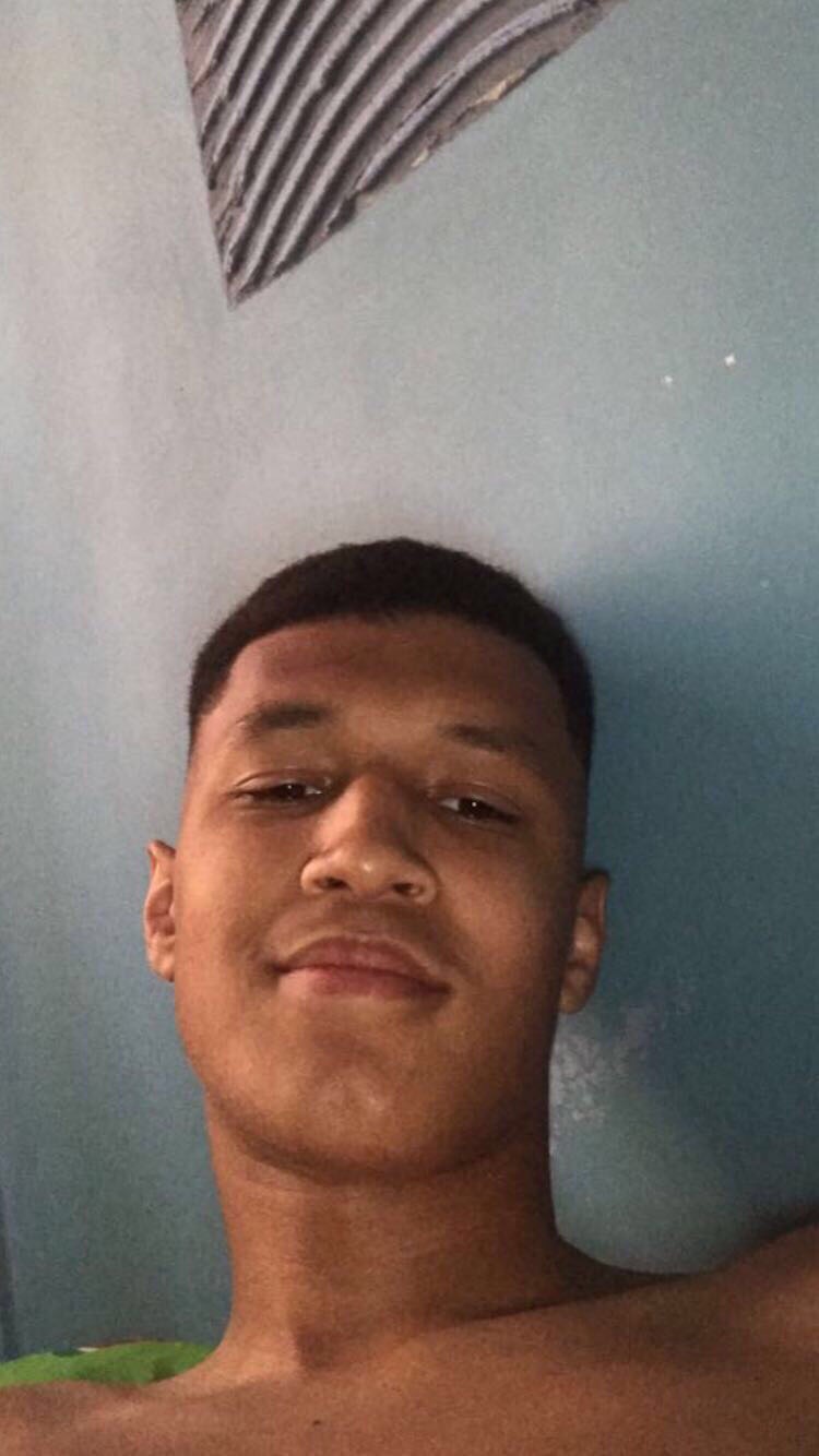 Portret młodego mężczyzny, ujęcie od dołu, widoczne fragmenty ramion, krótko ostrzyżone włosy, gładka skóra, tło stanowi ściana z widocznymi śladami malowania.