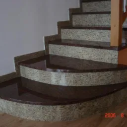 Granitowe schody wewnętrzne z zaokrąglonymi stopniami, wykończone ciemnym granitem, widok z dołu.