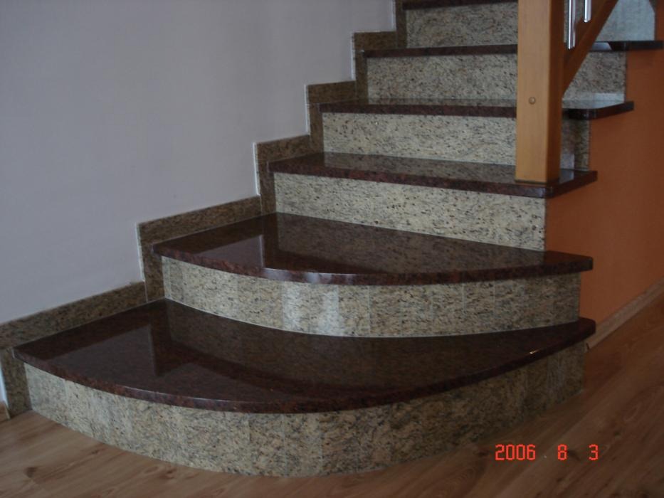 Granitowe schody wewnętrzne z zaokrąglonymi stopniami, wykończone ciemnym granitem, widok z dołu.