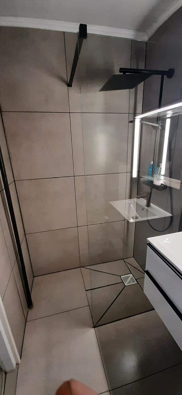 Nowoczesna łazienka z szarymi płytkami, czarną armaturą i odpływem liniowym w kształcie kwadratu.