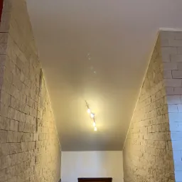 Wnętrze korytarza z dekoracyjną ścianą z kamienia, gładkim sufitem z oświetleniem punktowym i widoczną drabiną w tle.