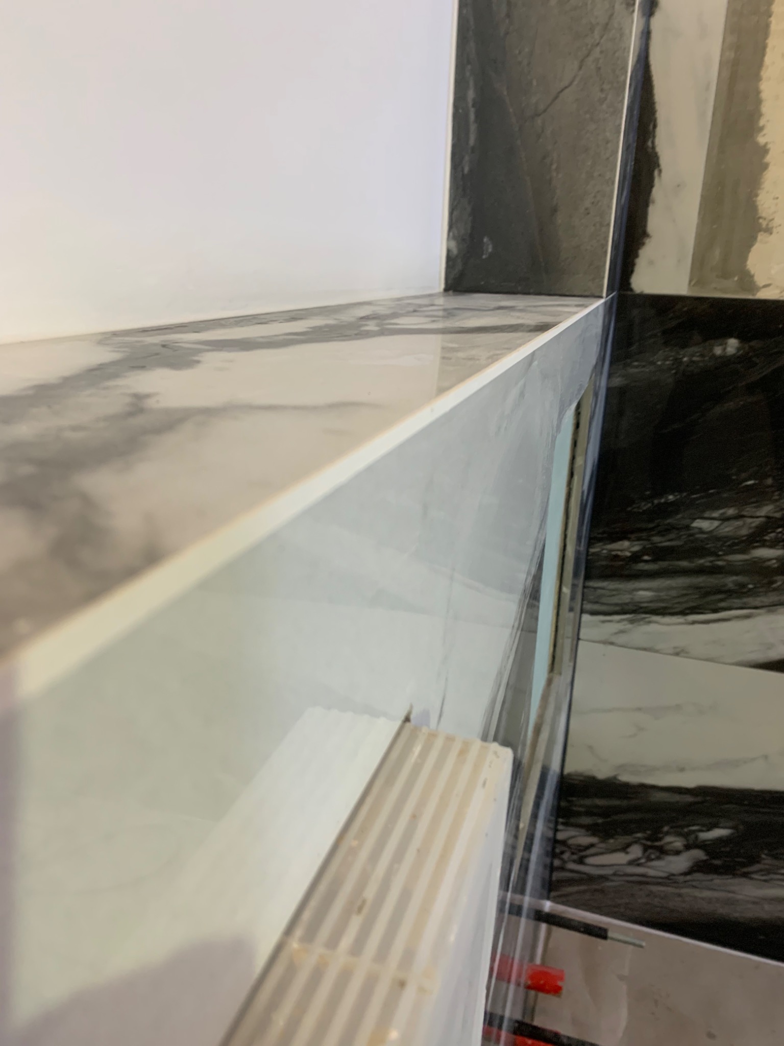 Fragment narożnika łazienki z ułożonymi płytkami imitującymi marmur w odcieniach szarości i bieli, widoczne elementy systemu poziomowania płytek.