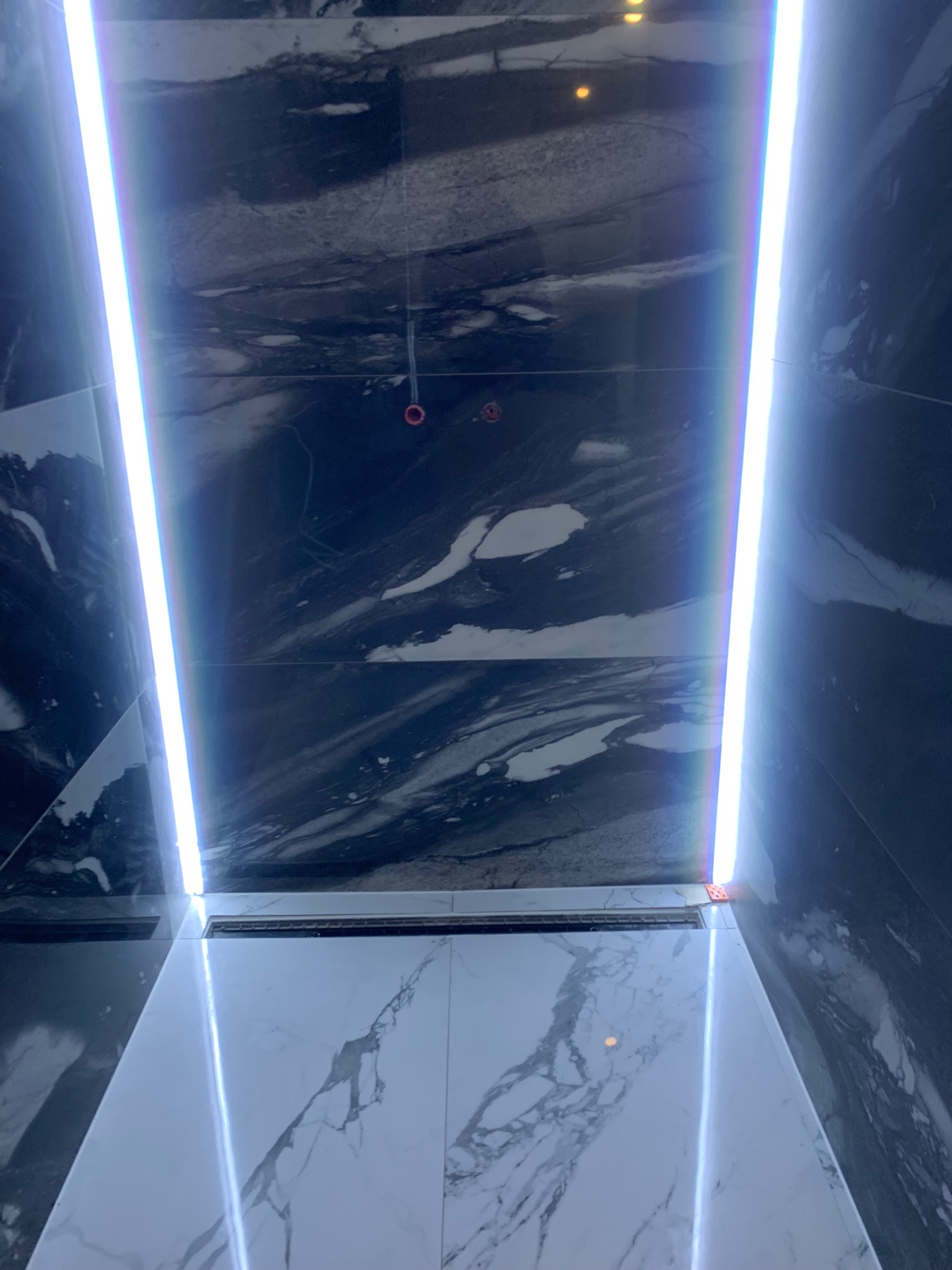 Wykończona łazienka z czarno-białymi marmurkowymi płytkami, oświetleniem LED w suficie i odpływem liniowym pod prysznicem.