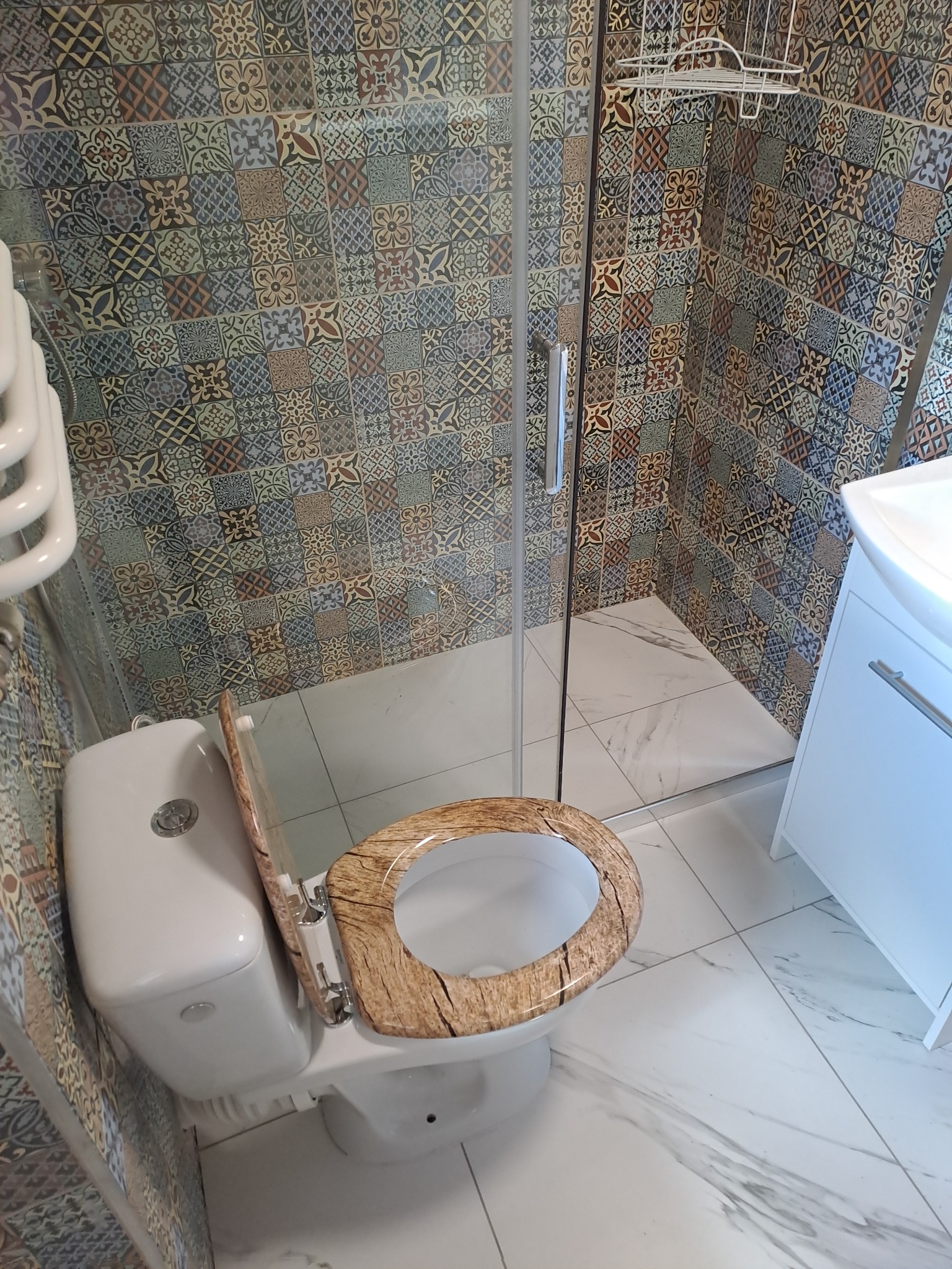 Wykończona łazienka z toaletą z deską imitującą drewno, kabiną prysznicową i patchworkowymi płytkami na ścianach.