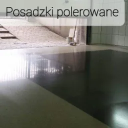 Częściowo wypolerowana posadzka w pomieszczeniu z białymi płytkami ściennymi i otwartym przejściem na zewnątrz z widocznymi schodami.