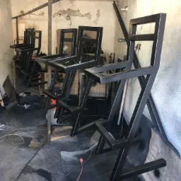 Surowe, czarne, geometryczne krzesła barowe wykonane z metalowych profili, wiszące na linkach w warsztacie podczas schnięcia farby.