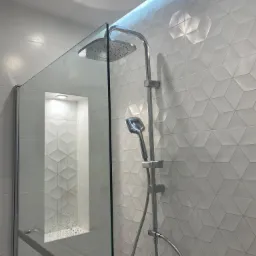 Nowoczesna kabina prysznicowa z deszczownicą i szklaną ścianką, białe trójwymiarowe płytki na ścianach, oświetlenie LED w niszy i na suficie.