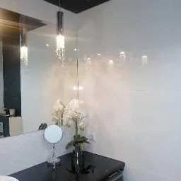 Białe płytki ścienne w łazience z czarnym blatem, lustro z podświetleniem, umywalka i bukiet białych kwiatów w wazonie