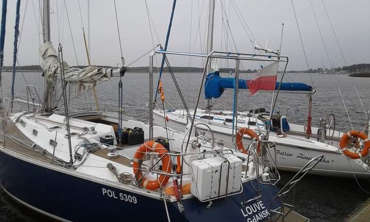 Dwa jachty żaglowe zacumowane w porcie, jeden z polską flagą na maszcie, widoczne koła ratunkowe i sprzęt pokładowy.