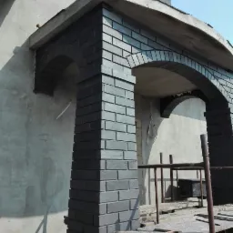 Murowany, ciemnoszary portal wejściowy z łukami w trakcie budowy, widoczne rusztowania i surowy tynk na ścianie budynku.