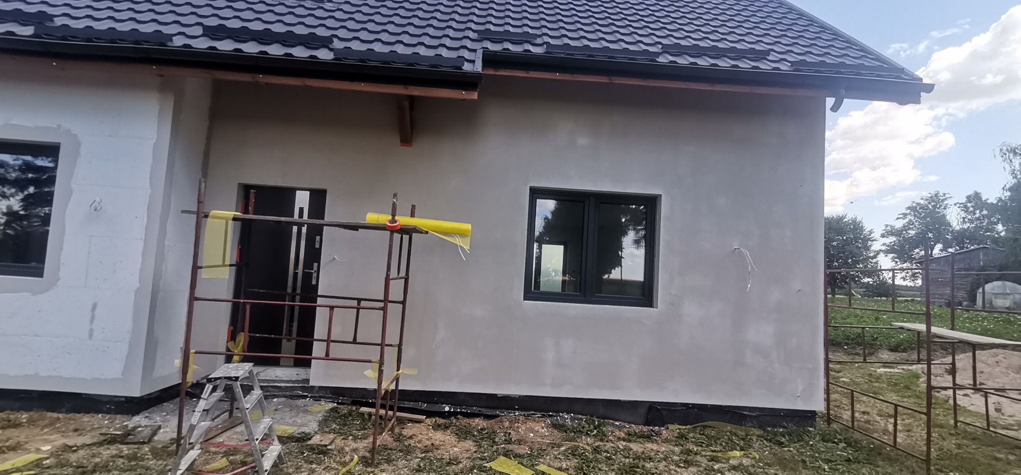 Dom w Nowym Mieście Lubawskim w trakcie prac elewacyjnych; widoczne rusztowanie, częściowo ocieplona ściana oraz fragment elewacji z nałożonym tynkiem.