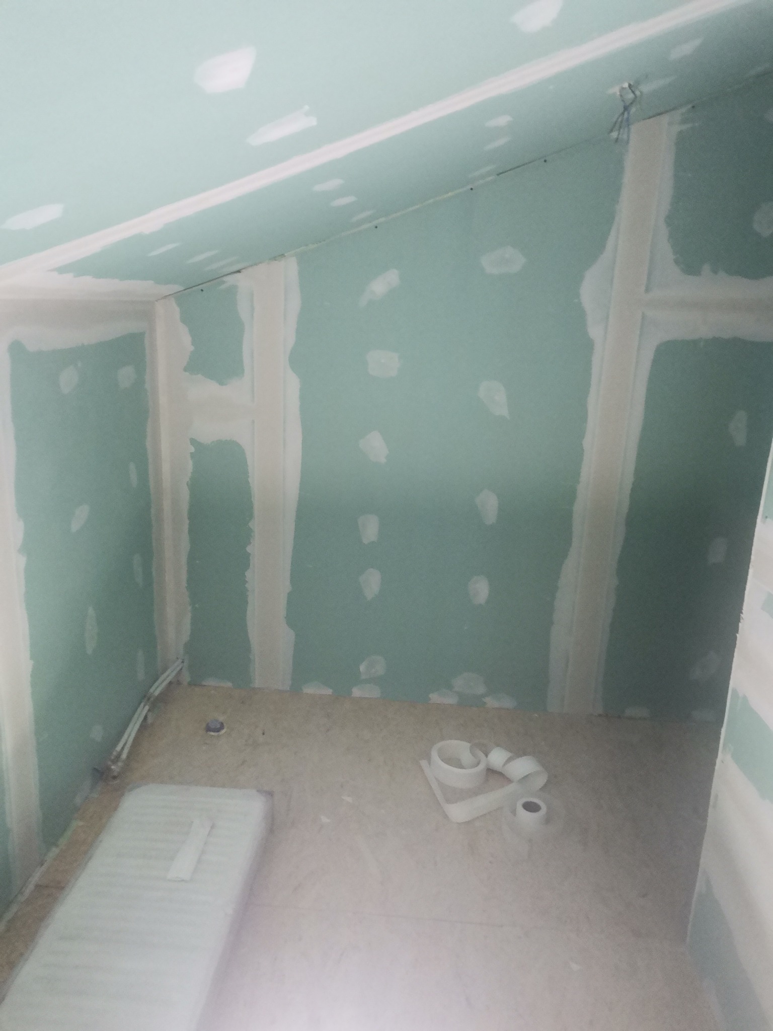 Wnętrze w trakcie montażu płyt kartonowo-gipsowych na ścianach i suficie, widoczne szpachlowane łączenia i taśma na podłodze.