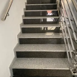 Schody z ciemnego i jasnego granitu, z metalową poręczą po prawej stronie, widok z góry na dół.