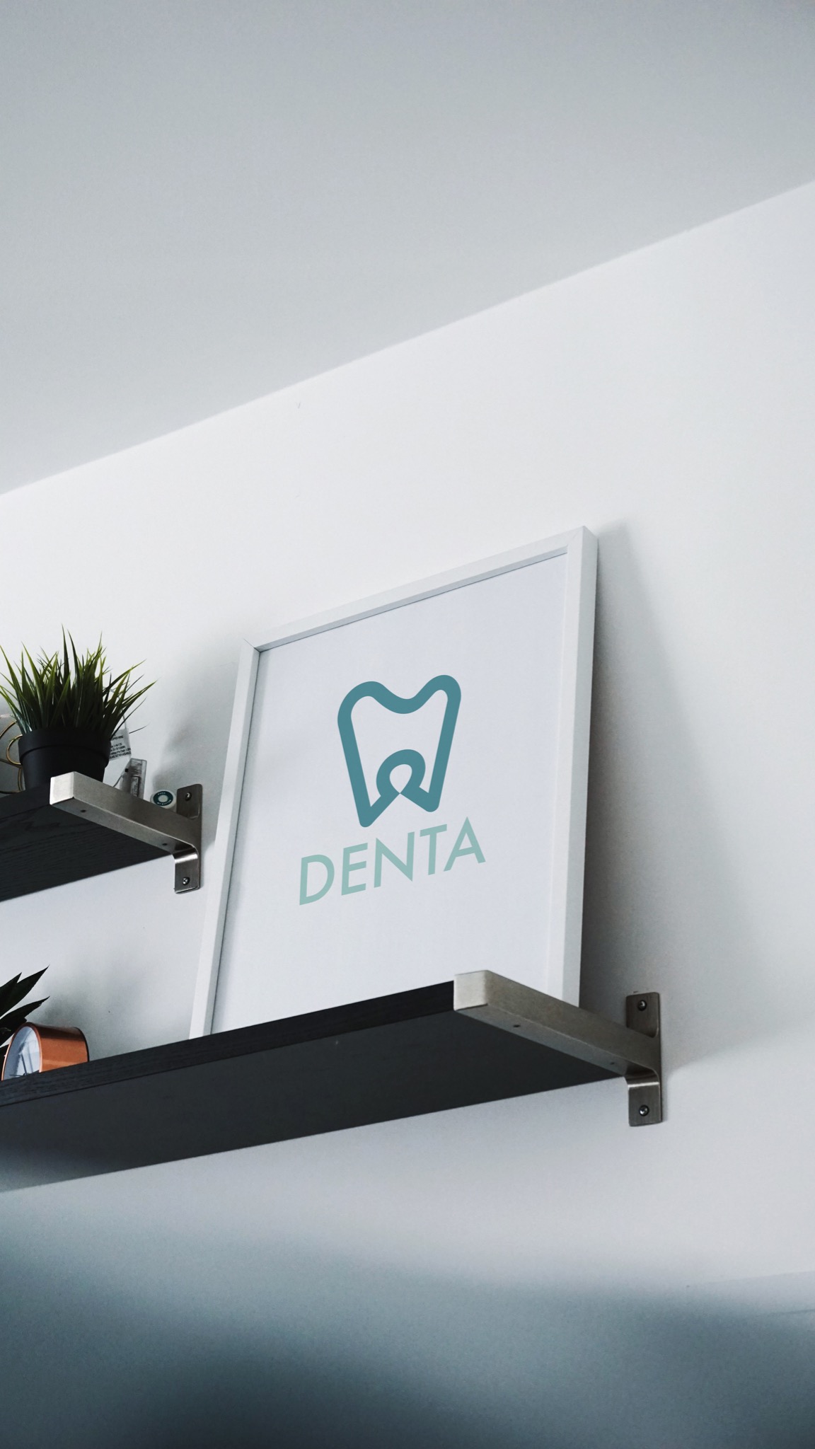 Oprawiony w ramkę, minimalistyczny projekt logo dentystycznego 'Denta' w odcieniach turkusu, umieszczony na półce w biurze.