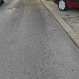 Kameleon Usługi Sprzątające i Ogrodnicze - Ulica miejska z rzędem zaparkowanych samochodów pod drzewami w słoneczny dzień, widok z perspektywy chodnika.