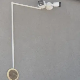 Zewnętrzny montaż dwóch kamer monitoringu na białym wysięgniku przy szarej ścianie budynku. Widoczny otwór wentylacyjny i okna z odbiciem.