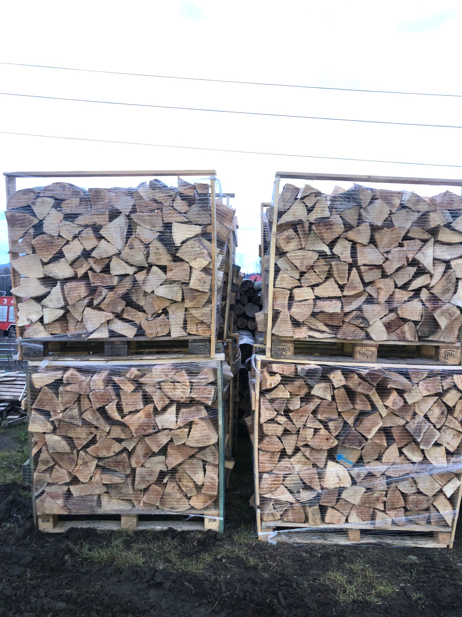 Dwa stosy pociętego drewna ułożonego w drewnianych skrzyniach na paletach, owinięte folią stretch.