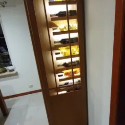 Drewniana witryna na wino z wewnętrznym oświetleniem LED, eksponująca butelki różnego rodzaju w minimalistycznym wnętrzu.