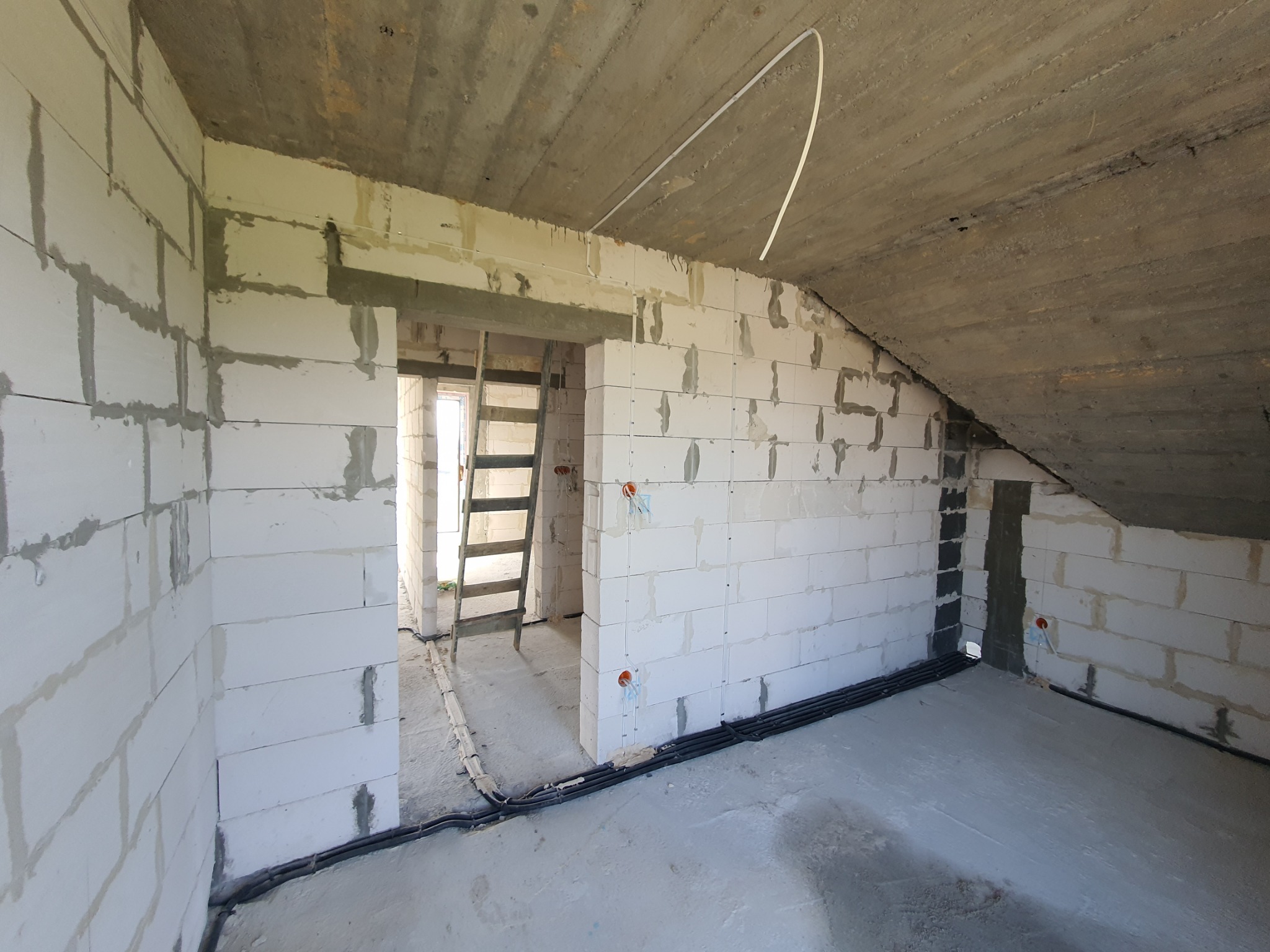 Surowy stan poddasza z widocznymi instalacjami elektrycznymi w peszlach, ściany z betonu komórkowego i betonowy strop przed wykończeniem.