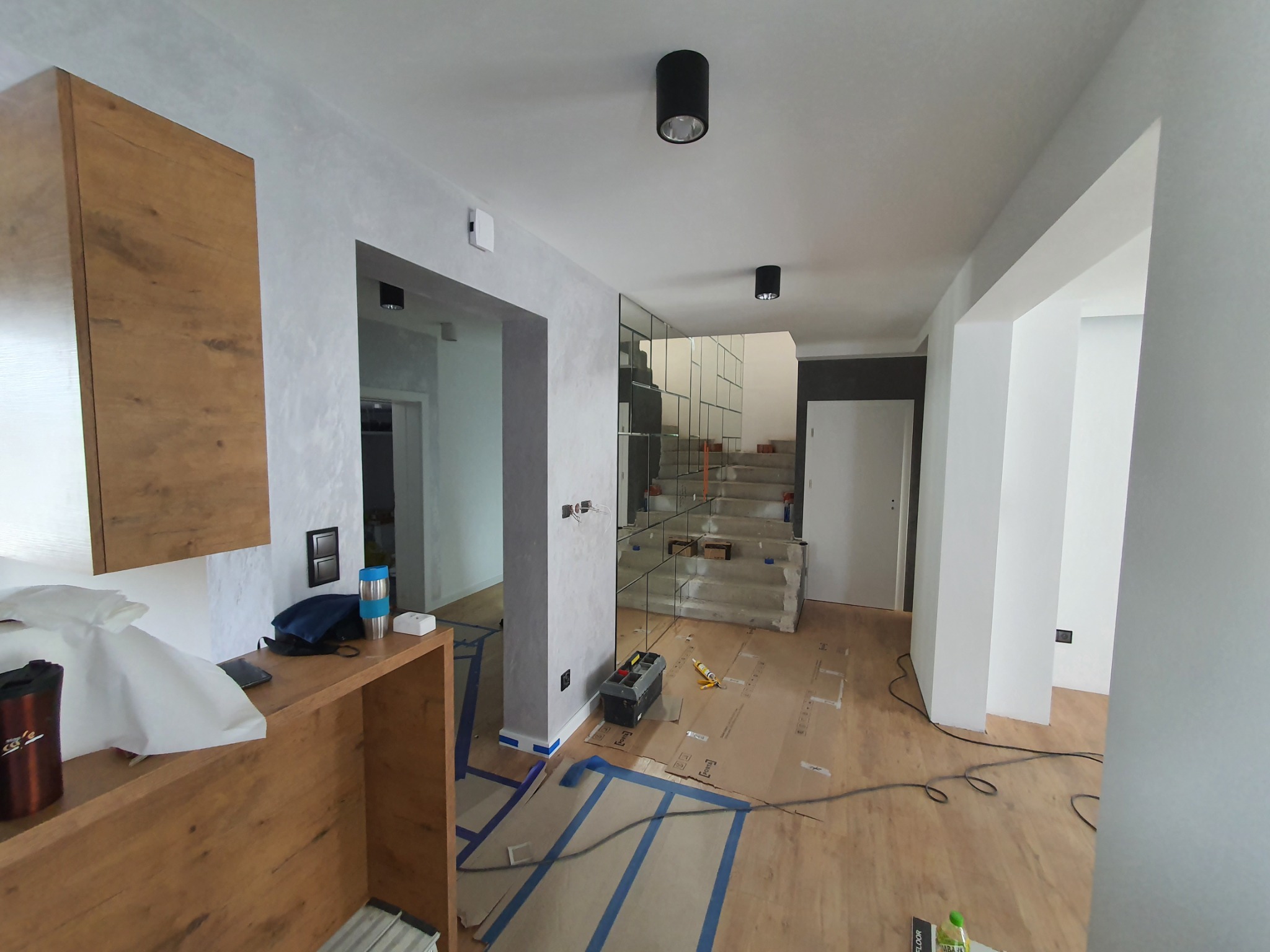 Wnętrze w trakcie prac wykończeniowych: zabezpieczona podłoga, widoczne narzędzia, schody z lustrzaną balustradą, zamontowane czarne lampy sufitowe.