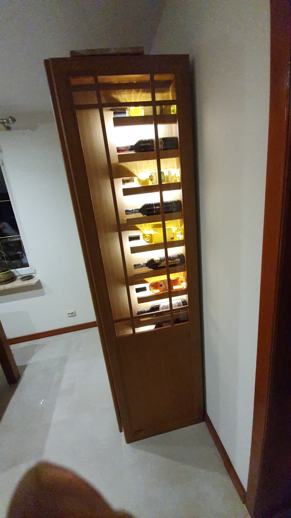 Drewniana witryna na wino z wewnętrznym oświetleniem LED, eksponująca butelki różnego rodzaju w minimalistycznym wnętrzu.