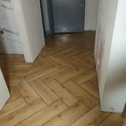 Andrzej Stachowski AMS - Nowo ułożona podłoga z paneli imitujących drewno w jodełkę, widoczna szara, zabezpieczona folią ochronną, metalowa futryna drzwi wejściowych do mieszkania z numerem 10, ściany w trakcie...