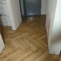 Nowo ułożona podłoga z paneli imitujących drewno w jodełkę, widoczna szara, zabezpieczona folią ochronną, metalowa futryna drzwi wejściowych do mieszkania z numerem 10, ściany w trakcie...