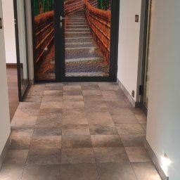 Andrzej Stachowski AMS - Hol z podłogą wyłożoną płytkami imitującymi kamień, z podświetlonymi stopniami i drzwiami z fototapetą przedstawiającą bambusowy las.