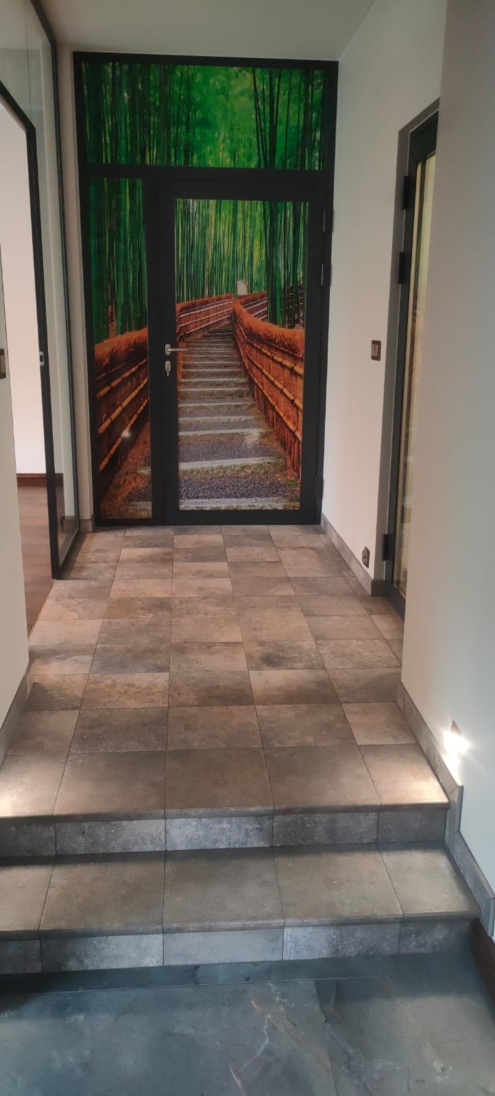 Hol z podłogą wyłożoną płytkami imitującymi kamień, z podświetlonymi stopniami i drzwiami z fototapetą przedstawiającą bambusowy las.