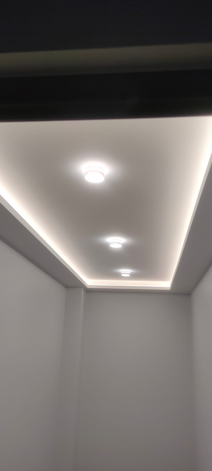 Nowoczesne oświetlenie sufitowe z trzema okrągłymi lampami i listwami LED w minimalistycznym wnętrzu z szarymi ścianami.