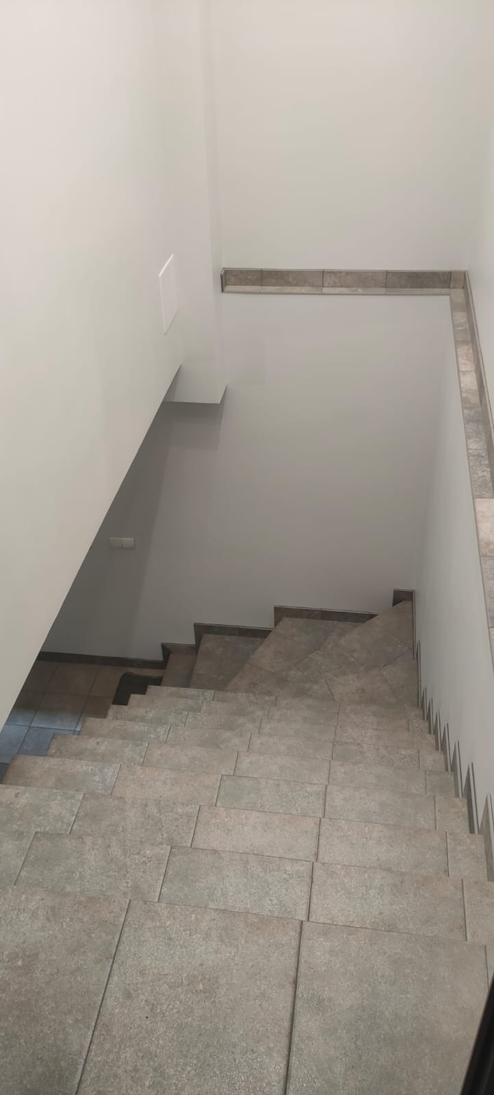 Schody wyłożone szarymi płytkami, widok z góry, z listwami przypodłogowymi z płytek.