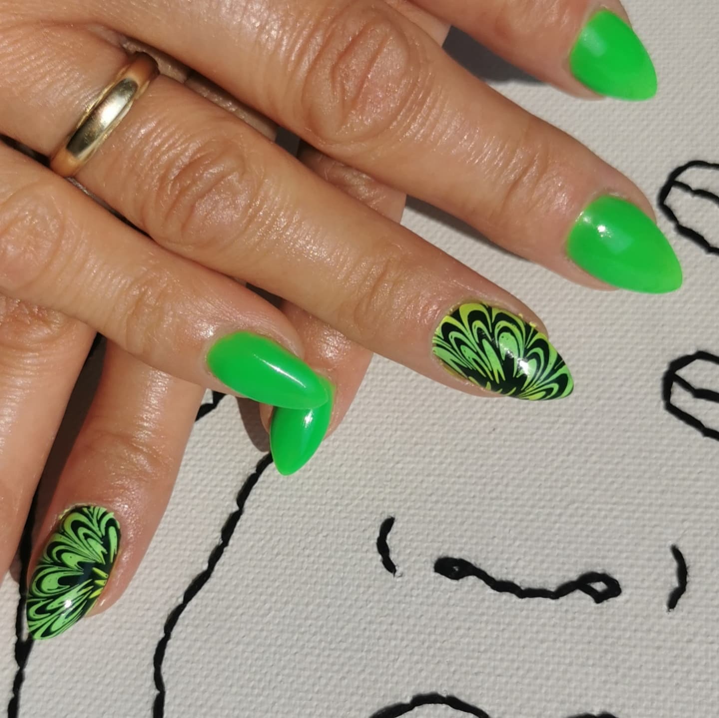 Dłoń z zielonymi, szpiczastymi paznokciami i wzorem w odcieniach zieleni i czerni, widoczny złoty pierścionek, usługa wykonana w Lesku.