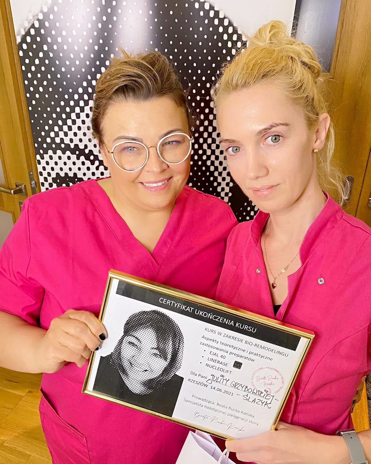Dwie kobiety w różowych uniformach prezentują certyfikat ukończenia kursu z zakresu bio-remodelingu, z widocznymi nazwami preparatów: EJAL 40, LINERASE, NUCLEOLIFT. Jedna z kobiet ma okulary...