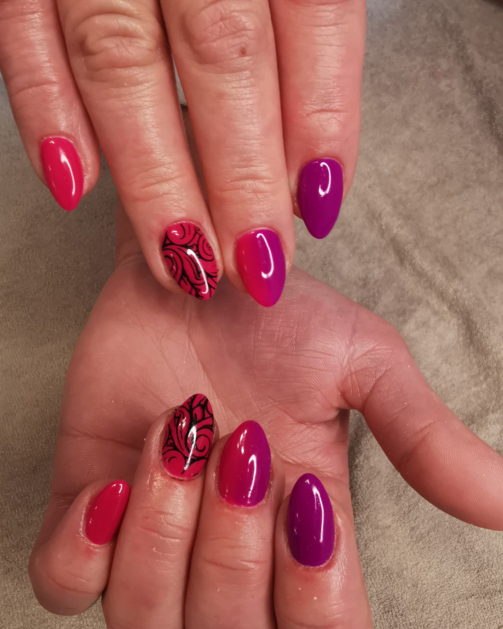 Dłonie z pomalowanymi na różowo i fioletowo paznokciami, z czarnym wzorem na dwóch paznokciach.