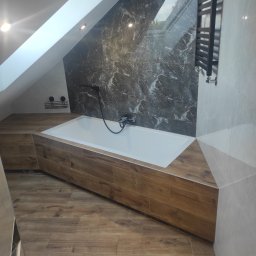 Dominik Miotk - Nowoczesna łazienka na poddaszu z wanną obudowaną panelami drewnopodobnymi, marmurową ścianą i grzejnikiem drabinkowym.