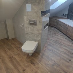 Dominik Miotk - Nowoczesna łazienka na poddaszu z drewnopodobnymi płytkami na podłodze i ścianach w strefie wanny, marmurowe płytki na ścianach przy toalecie, biała wisząca toaleta i okno dachowe w suficie.